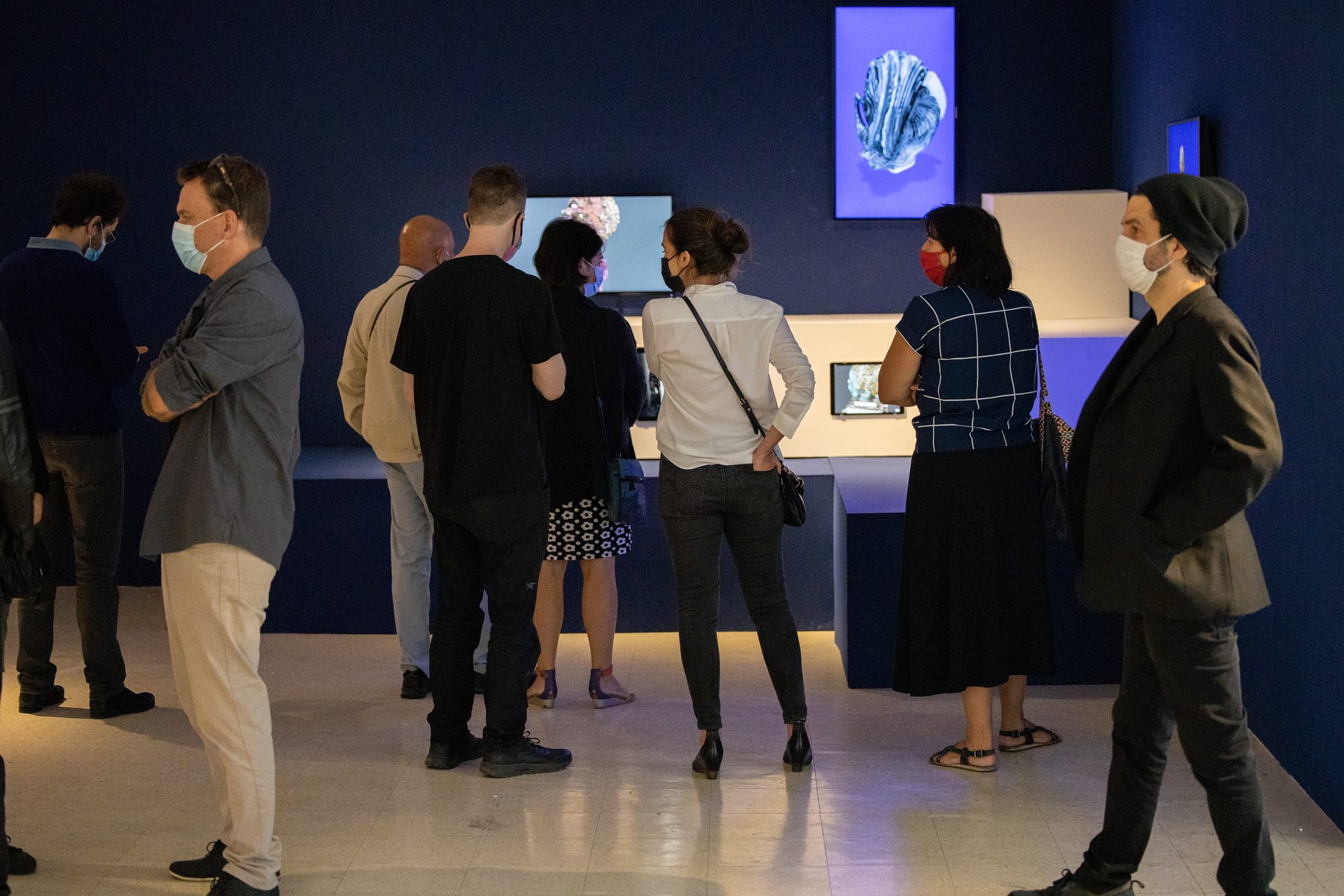 Opening night crowd in the blue-lit gallery at Art M&ucirc;r, visitors gathered around digital screens and sculptures