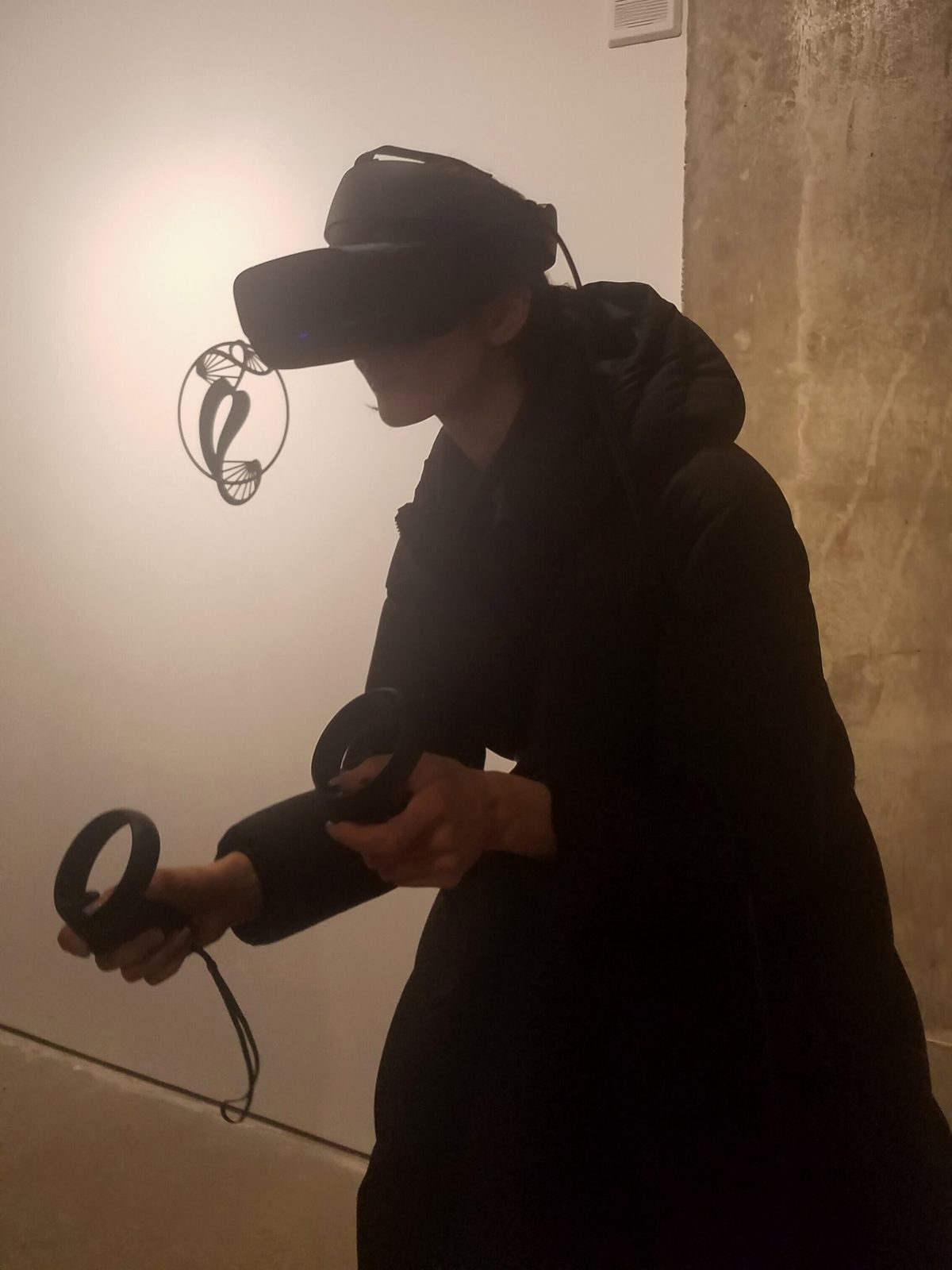 ELLEPHANT Gallery — dramatic silhouette of a visitor immersed in VR, holding controllers in darkness with the headset glowing
