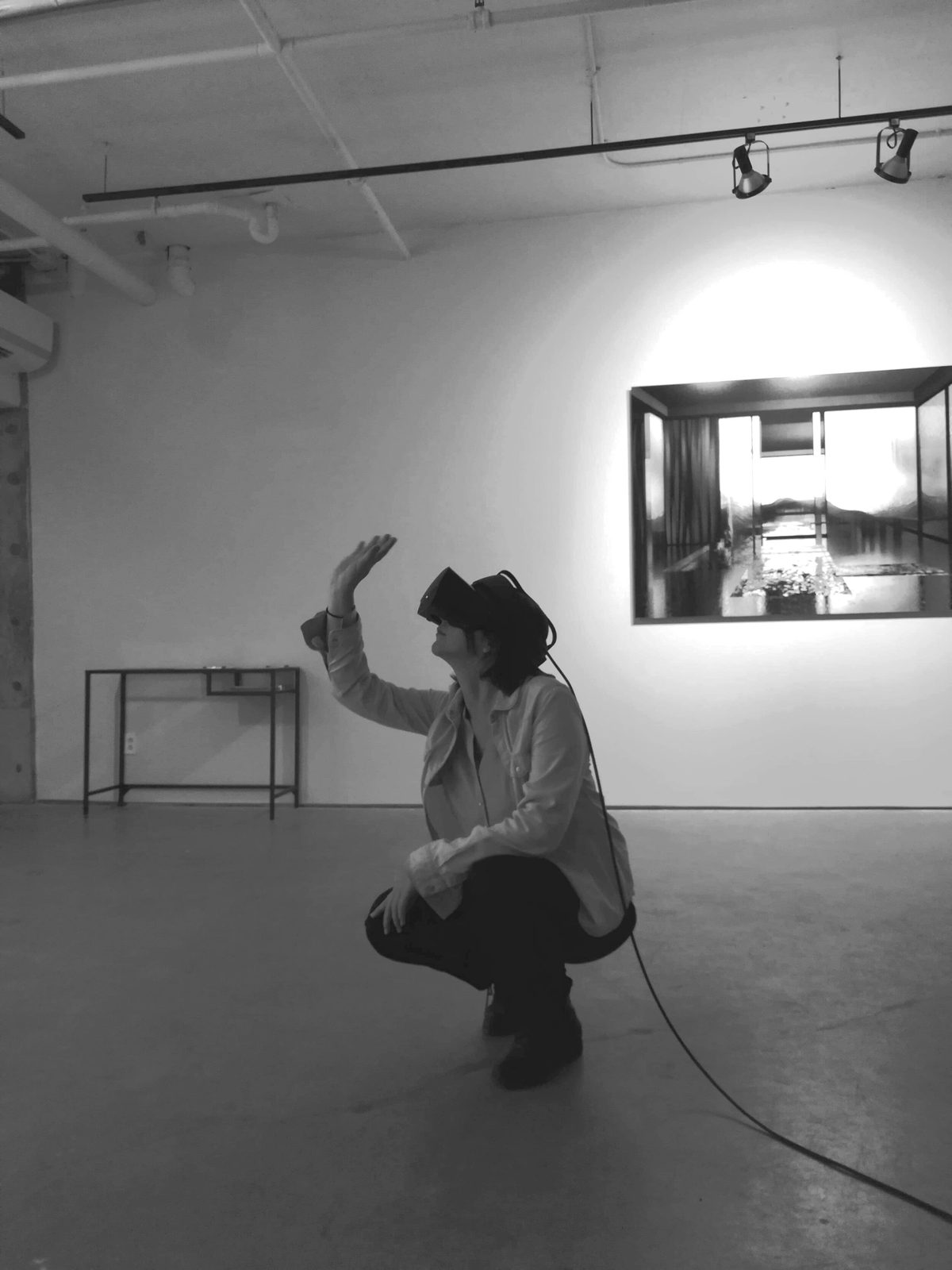 Salvo exhibition — visitor crouching and reaching upward while immersed in VR, black and white